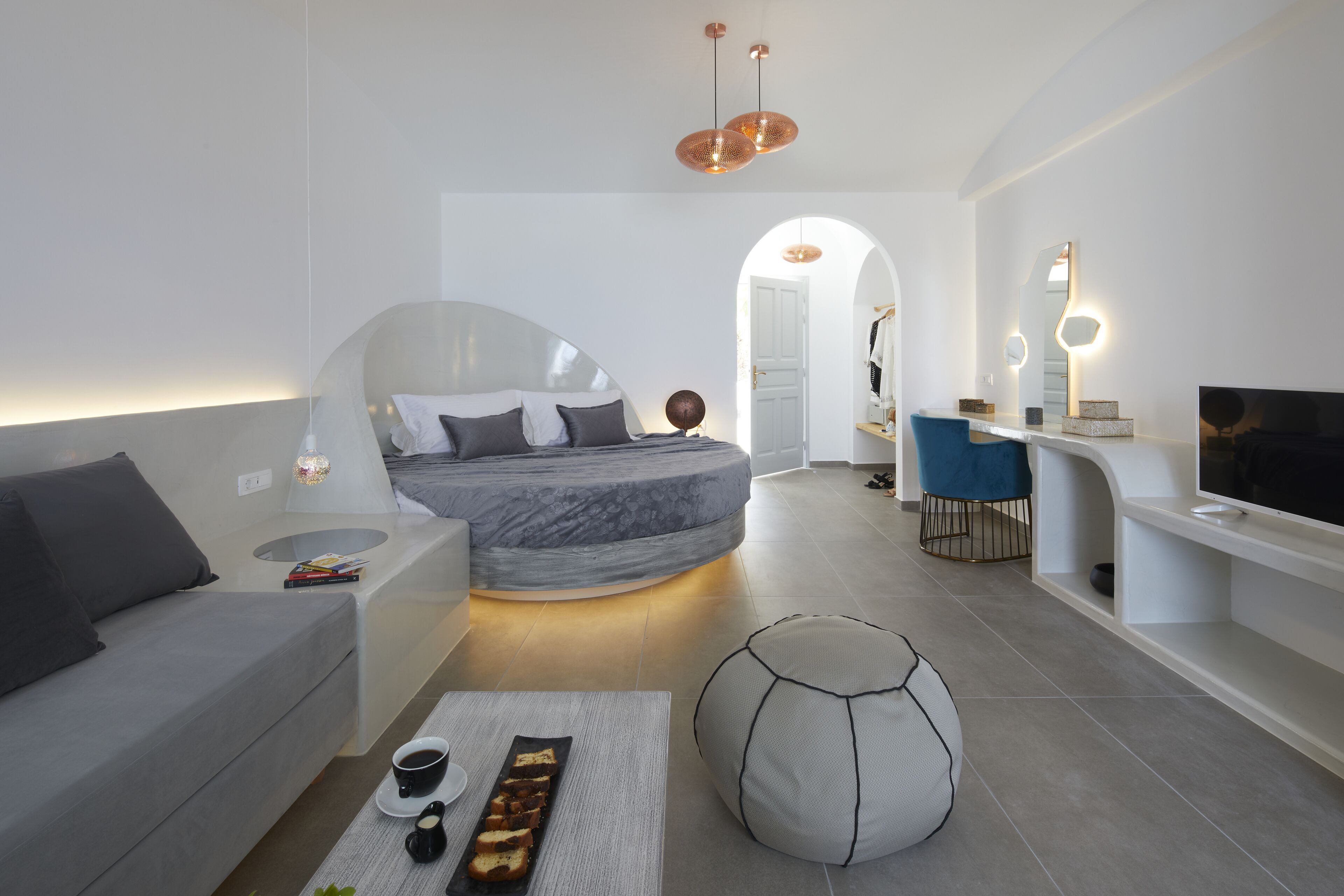 Un dormitorio moderno y minimalista con una cama curva, una zona de estar con una mesita de café y un televisor en un mueble empotrado.