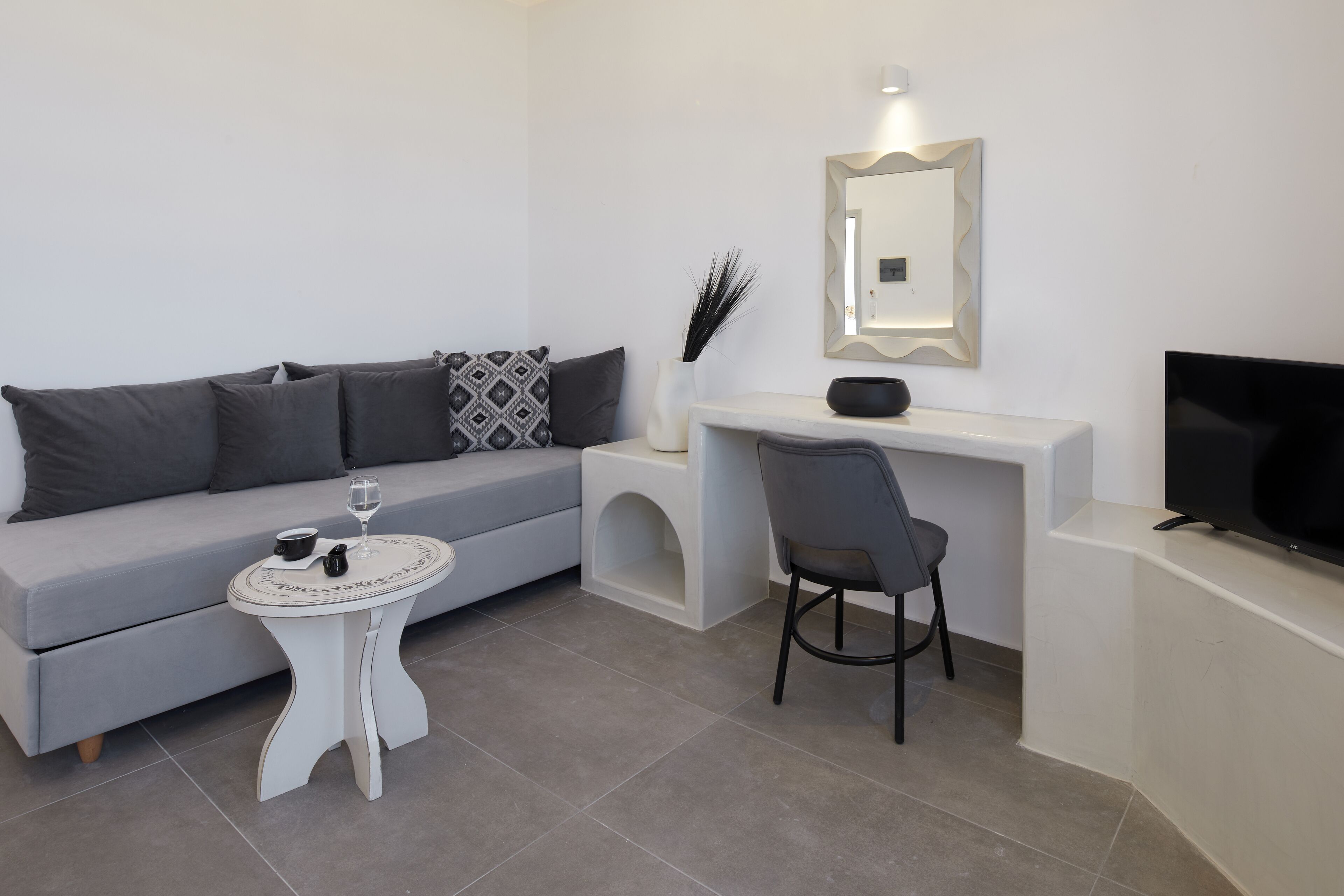 A modern living room with a grey sofa, a white coffee table, a grey chair, a flat-screen TV, and a small white table with a decorative bowl.