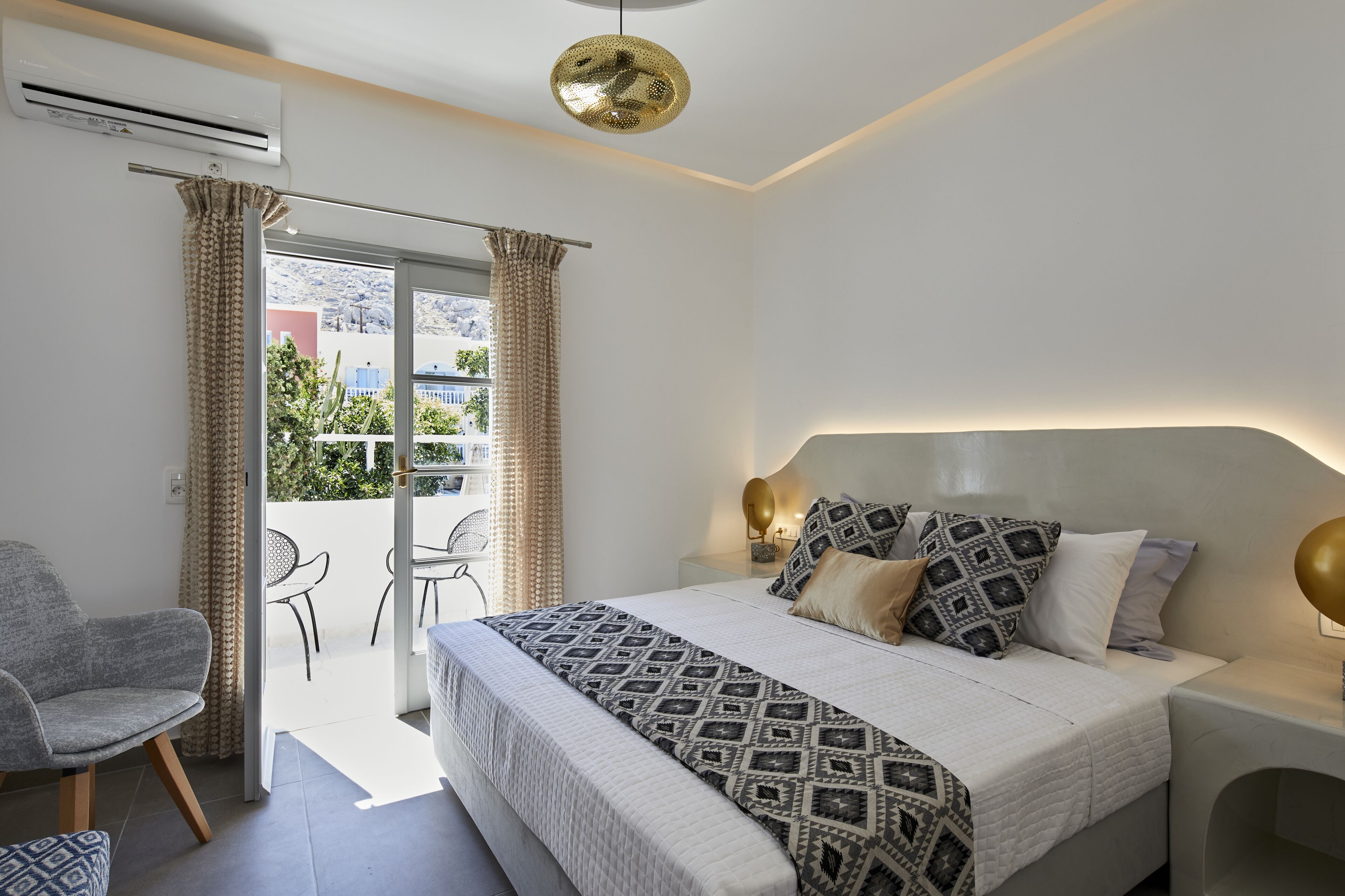 Een moderne slaapkamer met een groot bed, een stoel, een tafeltje en een balkon met gordijnen.