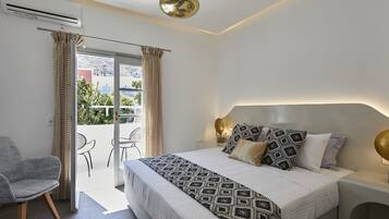 Ein modernes Schlafzimmer mit einem großen Bett, einem Sessel, einem kleinen Tisch und einem Balkon mit Vorhängen.