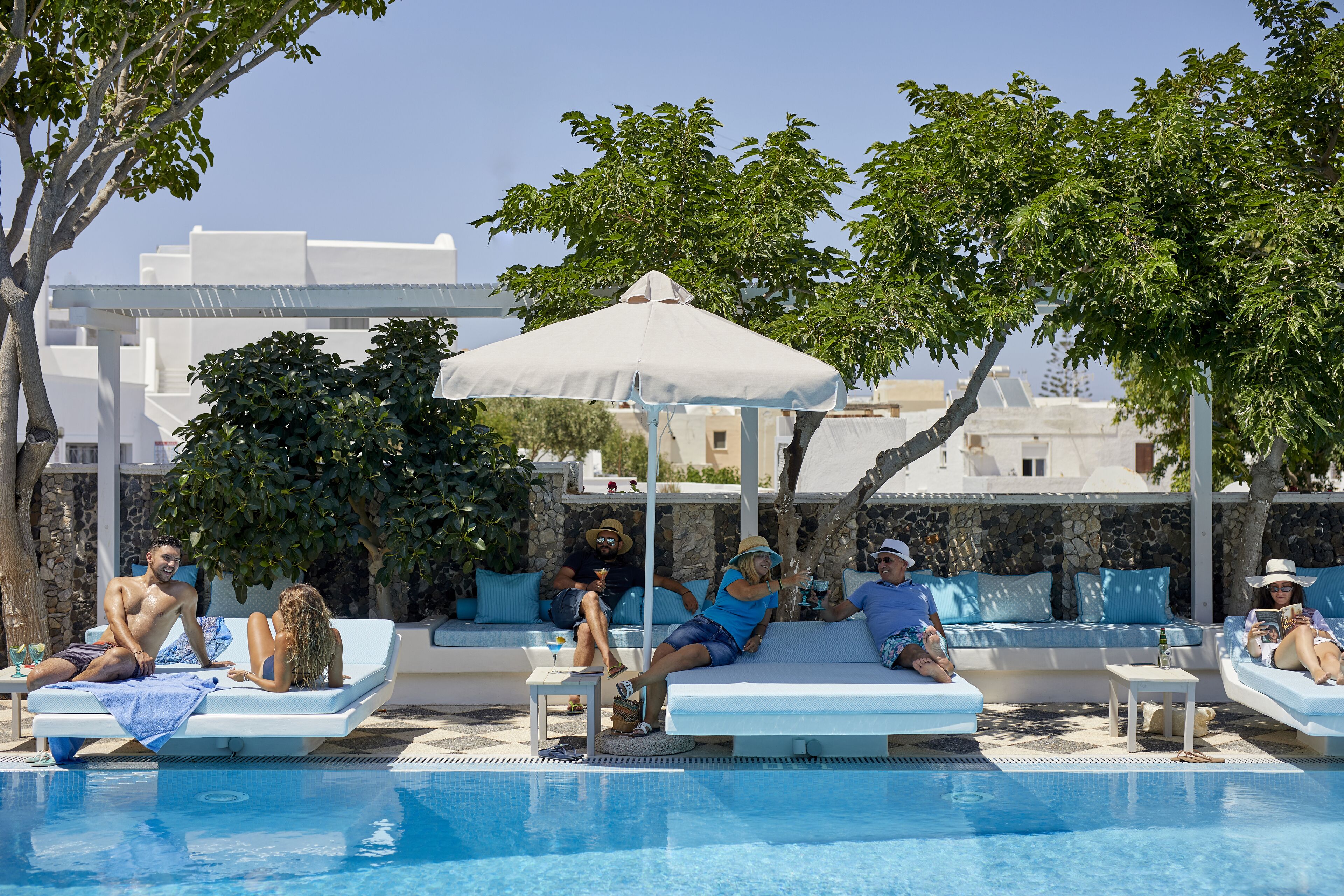 Zona junto a la piscina con sillas de descanso y sombrillas, rodeada de vegetación y muros de piedra.
