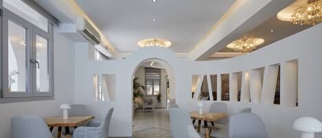 A modern dining area with wooden tables and chairs, a chandelier, and a view of the dining room in the background.