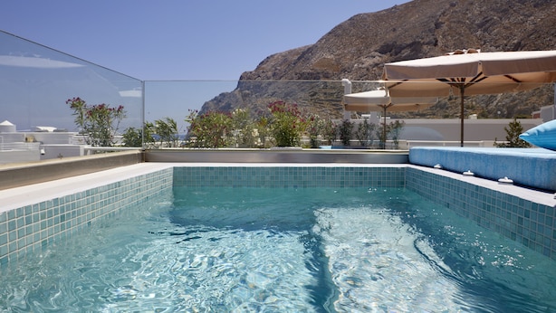 Una piscina con bordes de azulejos, rodeada de tumbonas y sombrillas, con montañas al fondo.