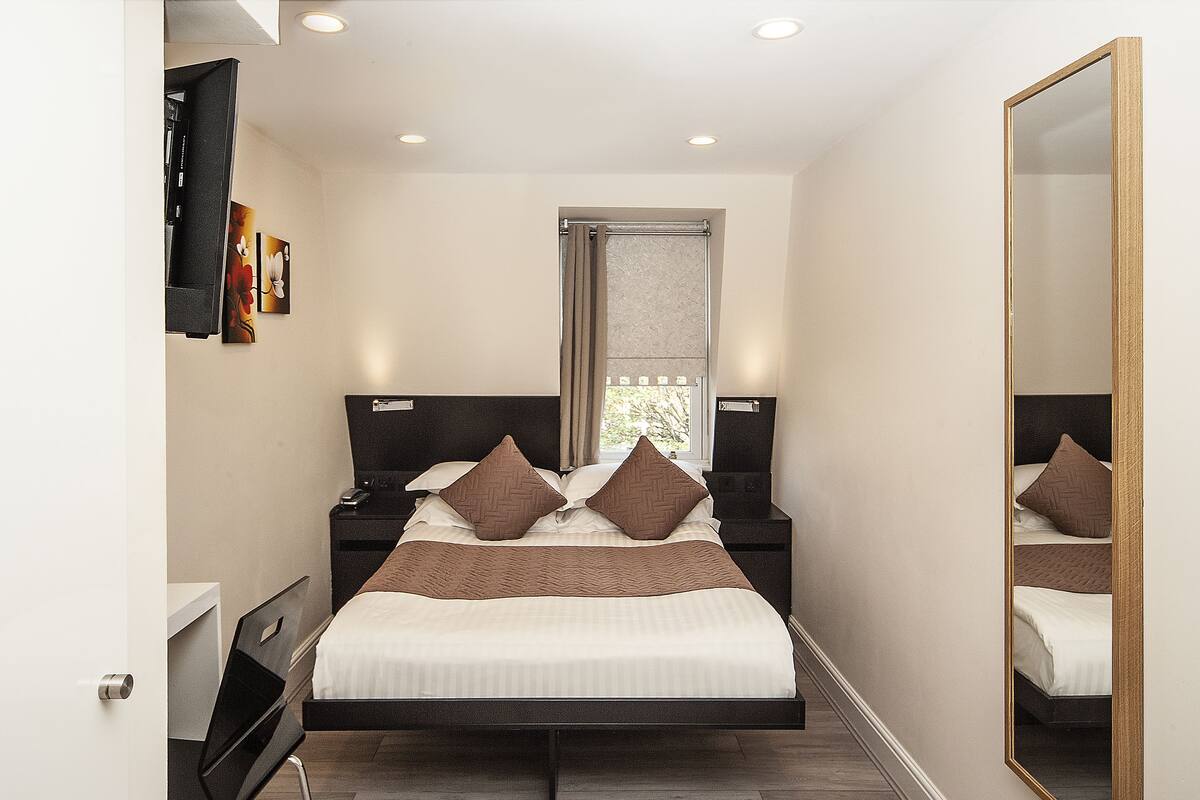 A modern bedroom with a bed, bedside tables, a mirror, and artwork on the wall.
