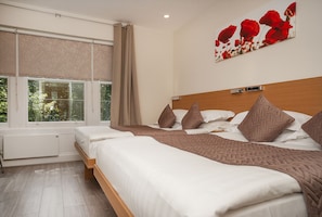 Een slaapkamer met een groot bed, een houten hoofdbord en een raam met uitzicht op groen.