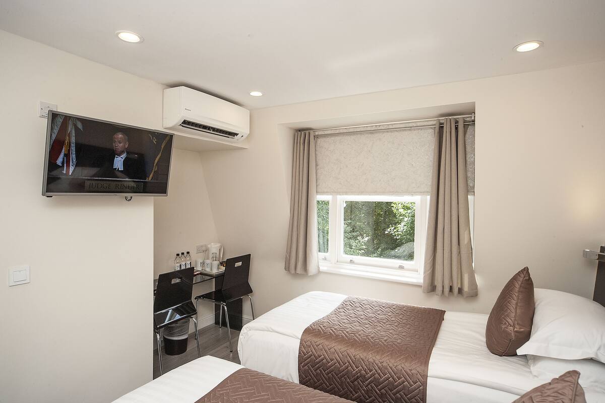 A hotel room with two beds, a desk with a chair, a television, and a window with curtains.