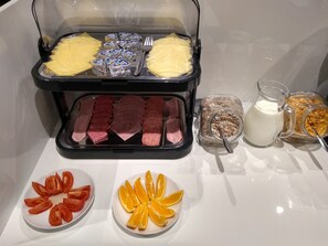 Een buffet met diverse soorten eten, zoals vleesschotels, kaas, fruit en drankjes.