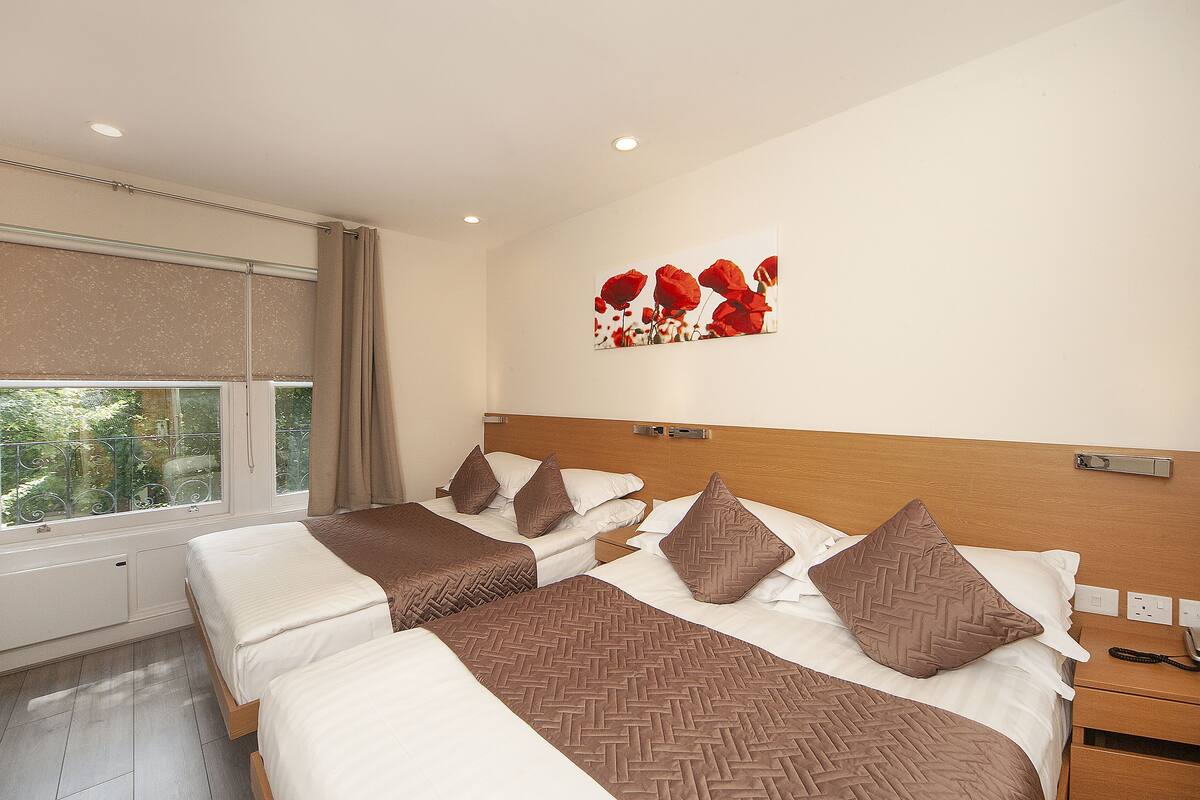 A hotel room with two beds, a wooden headboard, a window with blinds, and a wall-mounted artwork.