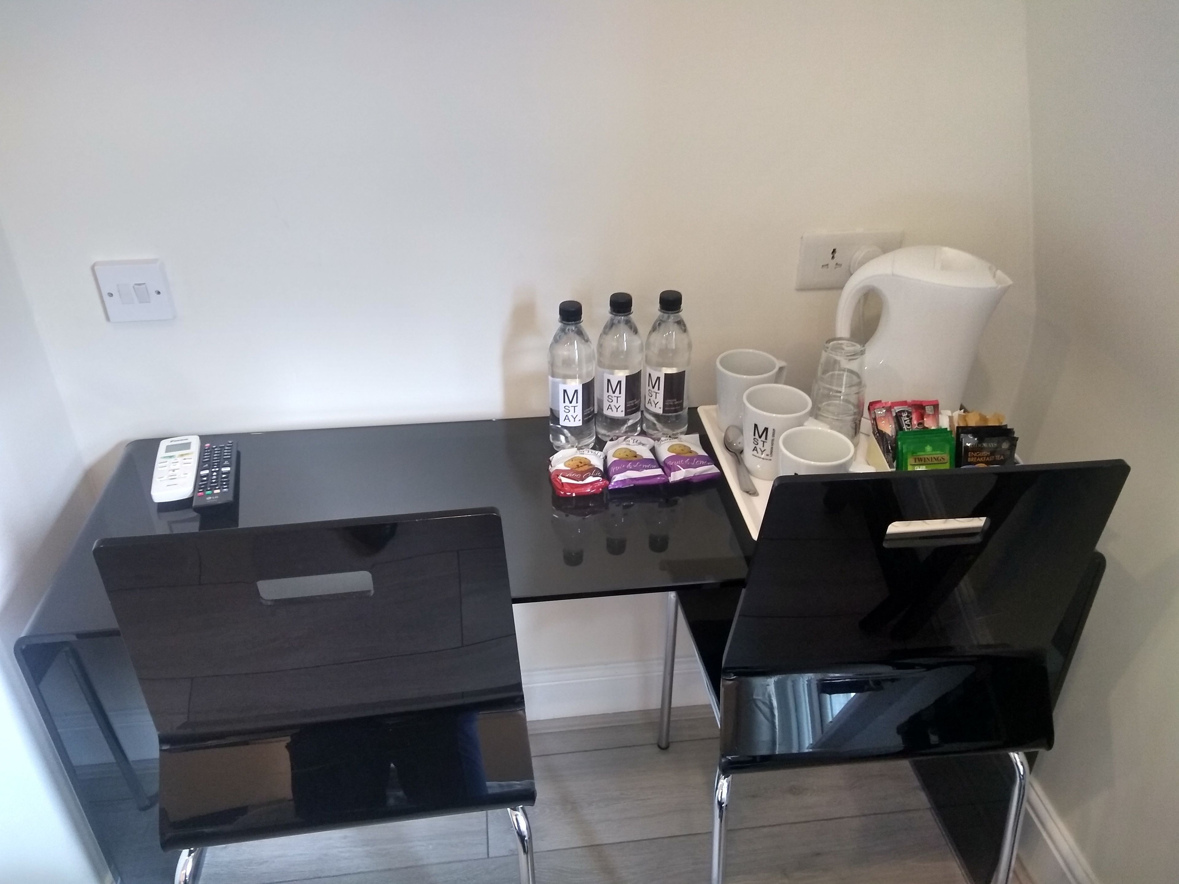Ein kleiner Essbereich mit einem schwarzen Tisch, zwei Stühlen, einer Fernbedienung, Wasserflaschen, Kaffeetassen und Snacks.