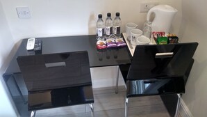 A small dining area with a black table, two chairs, a remote control, water bottles, coffee cups, and snacks. - Mstay Russell Court Hotel (London)