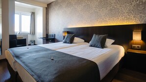 A hotel room with a large bed, two bedside tables with lamps, a small desk, and a window with curtains. - Hotel Ambassadeur (Ostend)