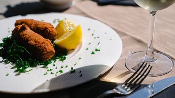 Une assiette de nourriture garnie d’une tranche de citron et d’herbes vertes, un verre de vin blanc et des couverts sur une table.