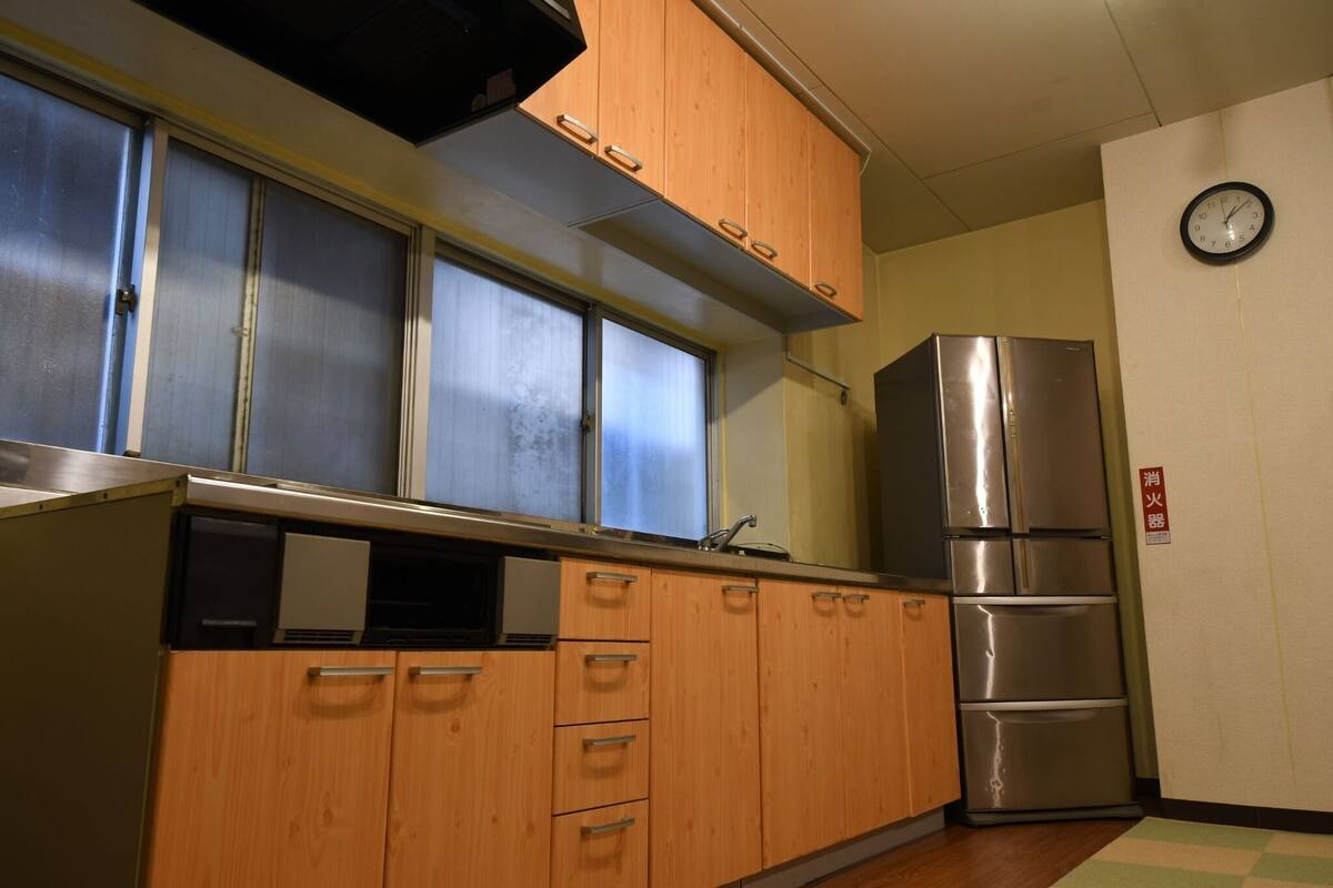 Een keuken met houten kastjes, een roestvrijstalen koelkast en een klok aan de muur.
