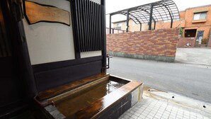 A wooden bench outside a building with a brick wall and a metal gate. - Onsen Yado Hamayu Nagi - Hostel (Beppu)
