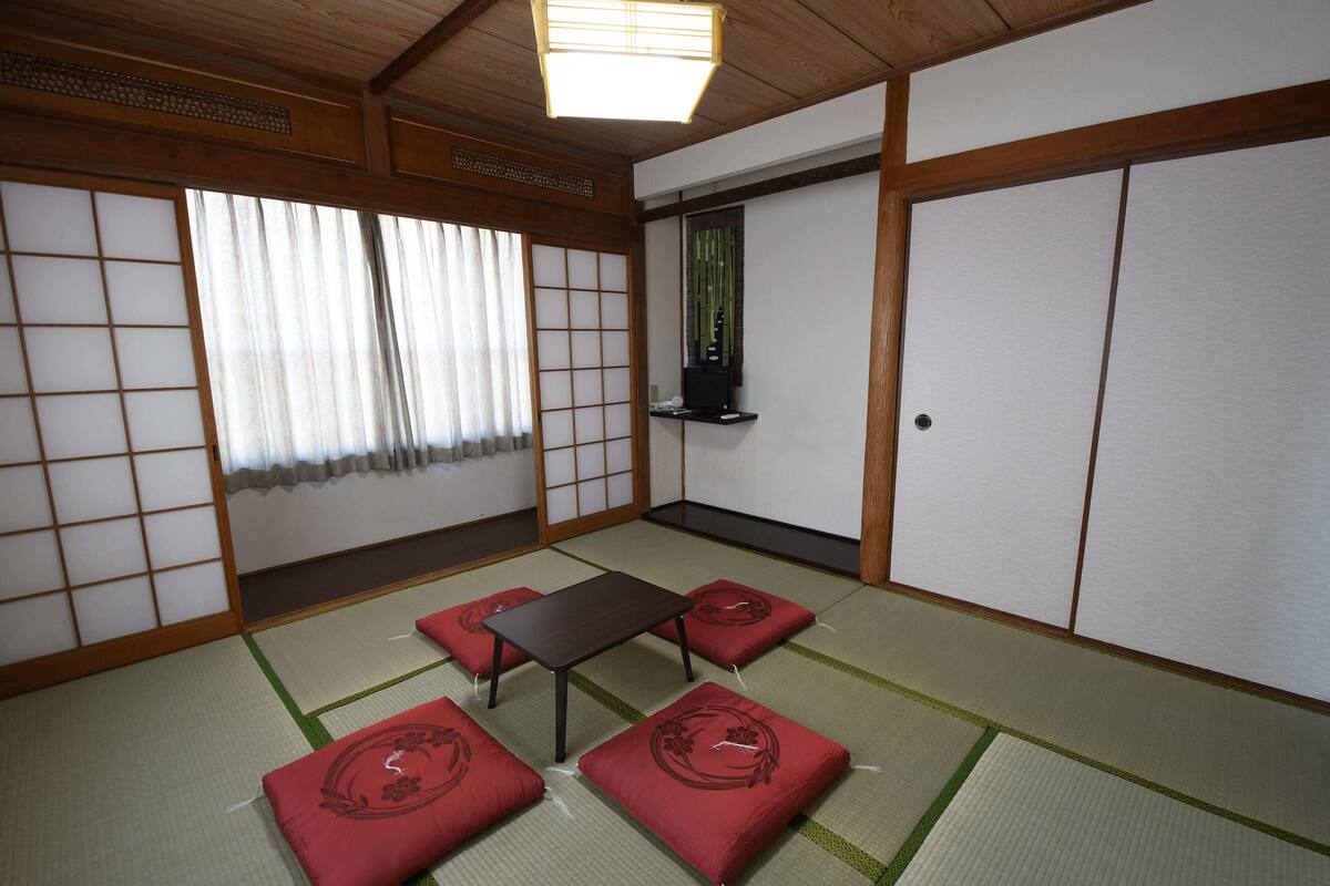 Een traditionele Japanse kamer met tatami vloerbedekking, een lage tafel en rode kussens.