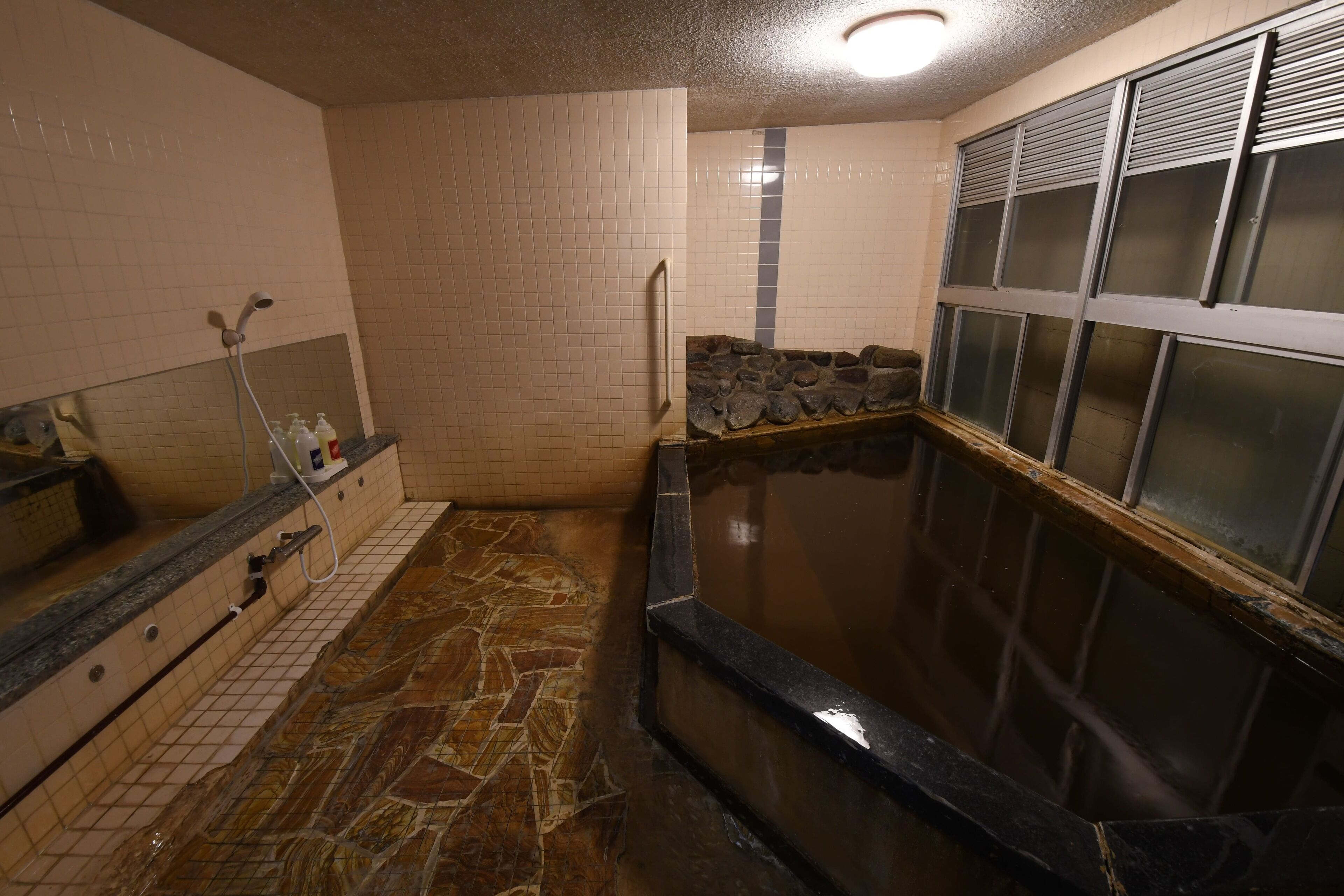 A spa area with a stone floor, a small pool, and a window with blinds.