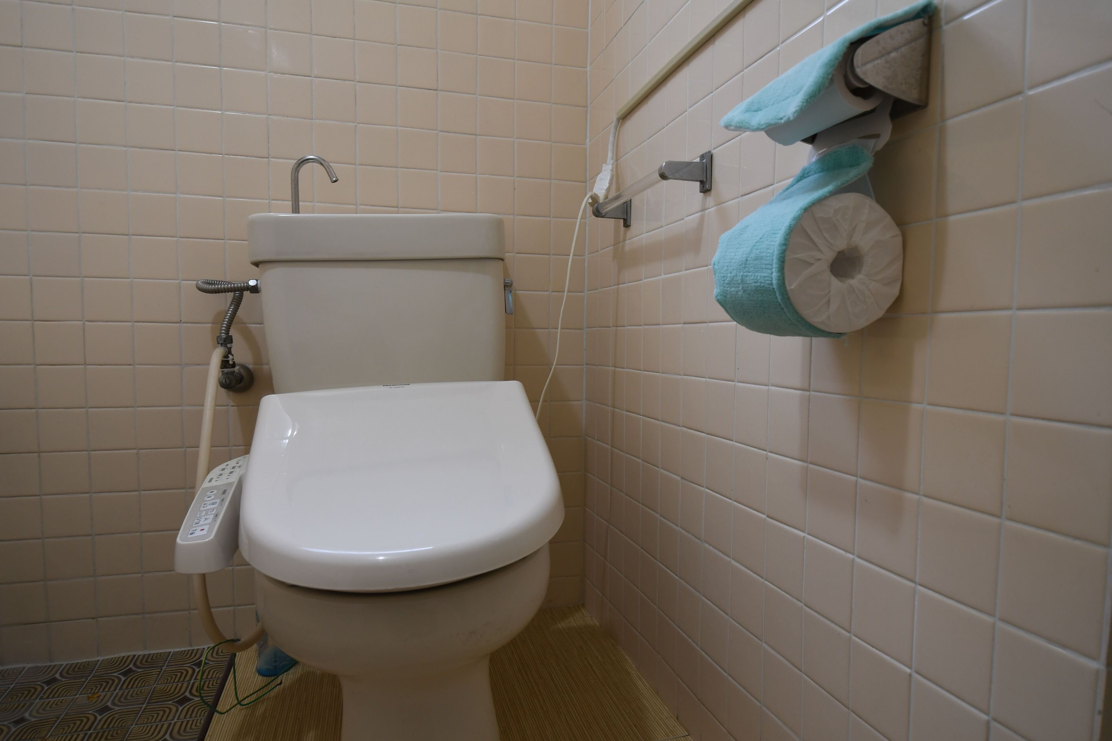 A toilet with a control panel, a towel dispenser, and a toilet paper holder on the wall.