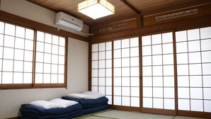 A traditional Japanese room with tatami flooring, a futon bed, sliding shoji doors, and a ceiling fan. - Onsen Yado Hamayu Nagi - Hostel (Beppu)