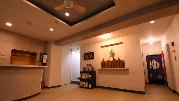 A hotel lobby with a reception desk, a ceiling fan, recessed lighting, a wall-mounted shelf with books, and a spa sign. - Onsen Yado Hamayu Nagi - Hostel (Beppu)