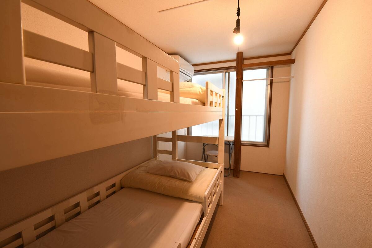 Een slaapkamer met stapelbed, raam en bureau.