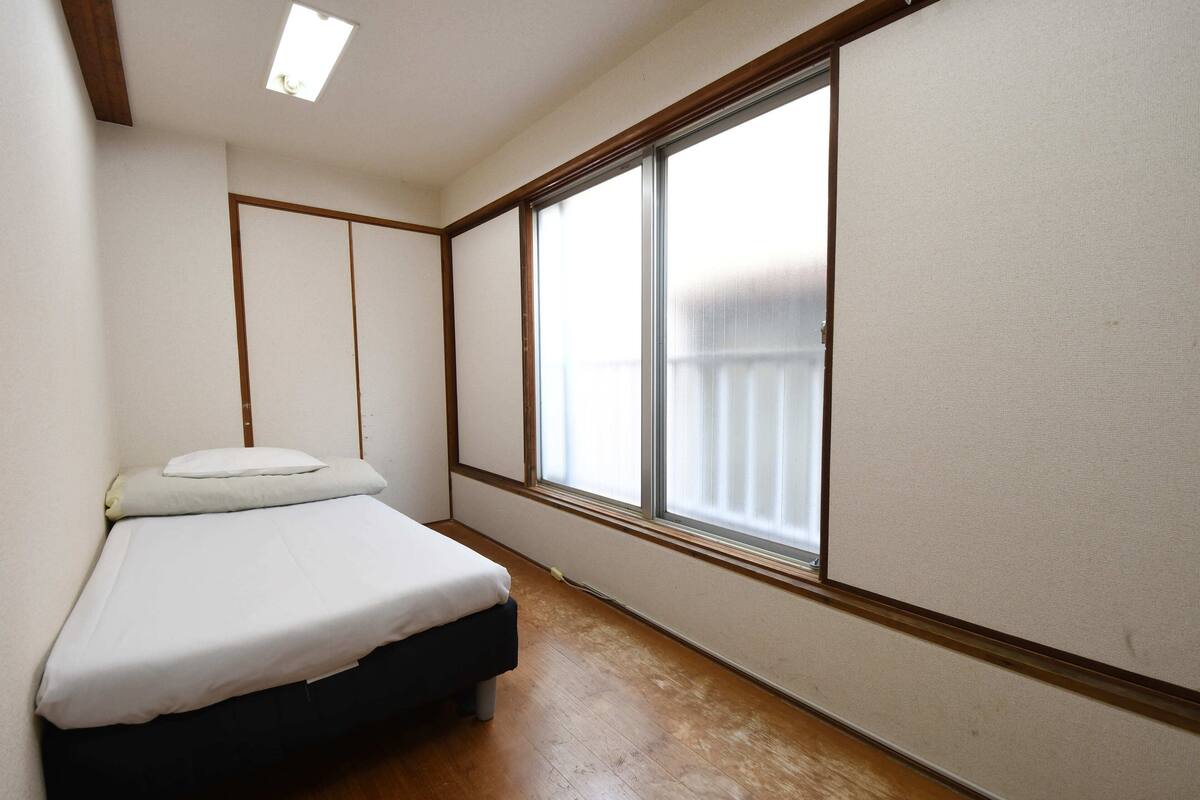 Een kamer met een bed, een groot raam en houten sierlijsten.