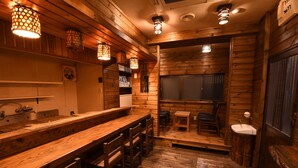 A wooden interior with a long counter, stools, and a sink. - Onsen Yado Hamayu Nagi - Hostel (Beppu)