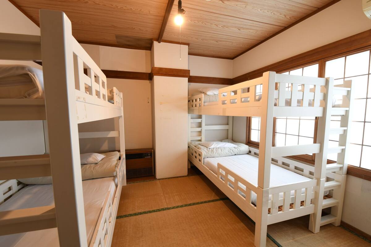 Een slaapkamer met een stapelbed, houten balken in het plafond, een raam met uitzicht en een kleine deur.