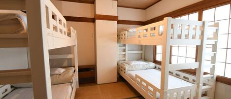 Une chambre avec des lits superposés, des poutres en bois au plafond, une fenêtre avec vue et une petite porte.