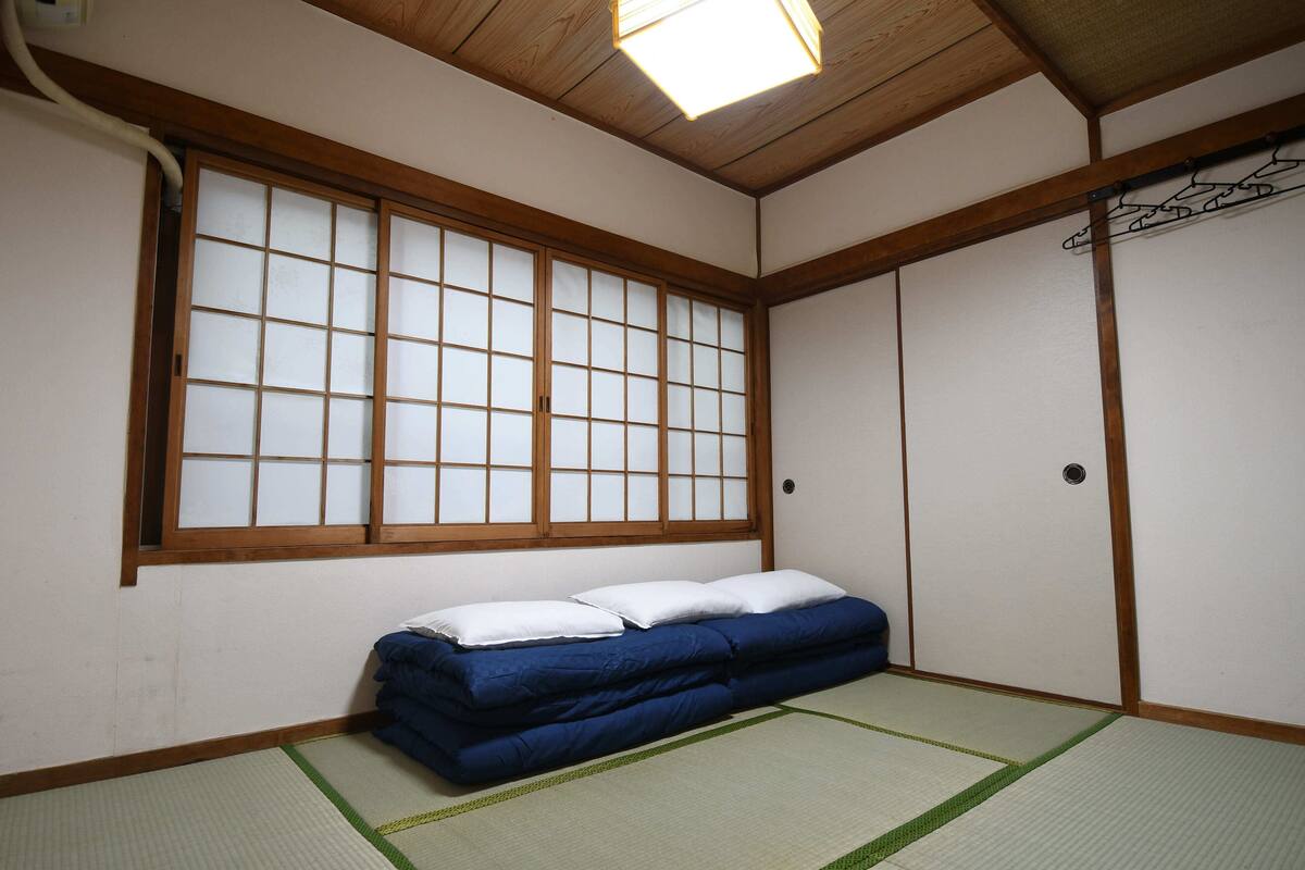 Een traditionele Japanse kamer met tatami vloerbedekking, een futon bed, shoji schuifdeuren en een hangende kledingrek.