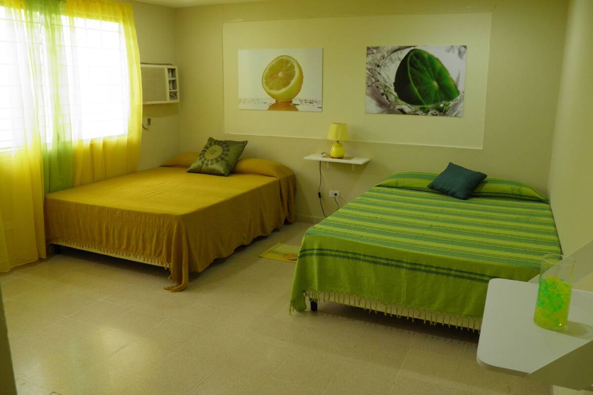 A room with two beds, a small table, and a wall-mounted air conditioner.