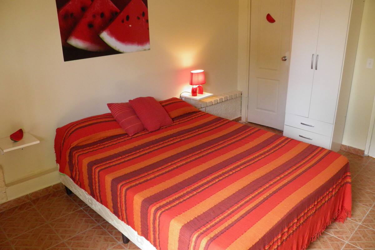 A bedroom with a bed, pillows, a nightstand, a lamp, a wardrobe, and a wall decoration.