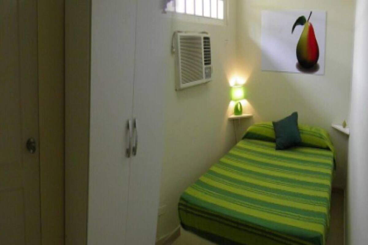 A bedroom with a bed, a wardrobe, an air conditioning unit, and a wall-mounted light.