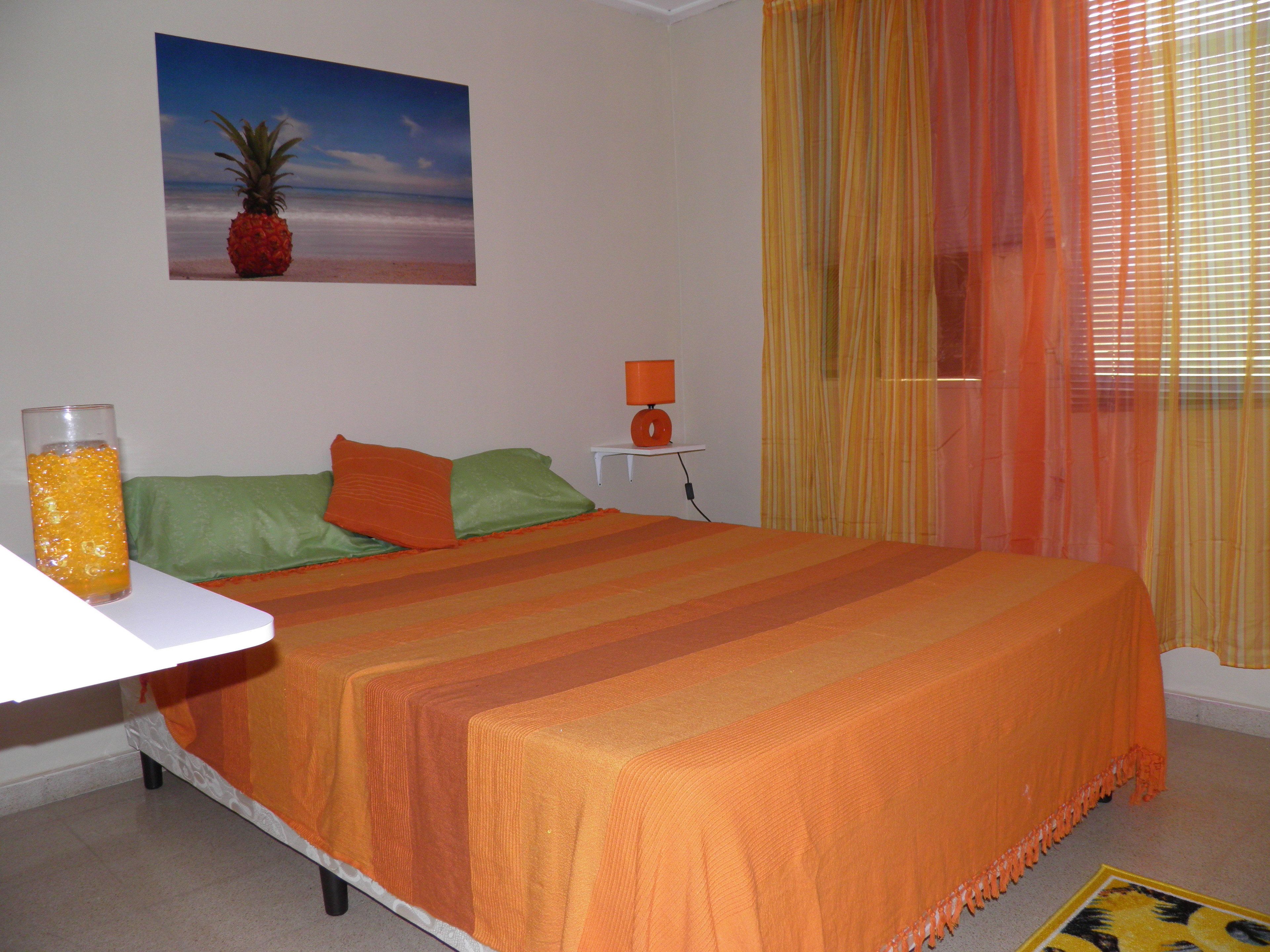 A bedroom with a bed, pillows, a nightstand, a lamp, a glass of orange juice, and a painting of a beach scene.