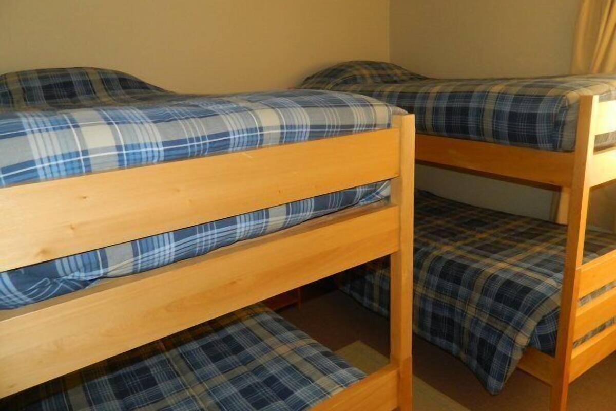 A bunk bed room with blue plaid bedding and wooden frames.