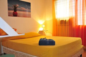 Ein Hotelzimmer mit einem Bett, einem Nachttisch, einer Lampe und einem Ananas-Gemälde an der Wand.