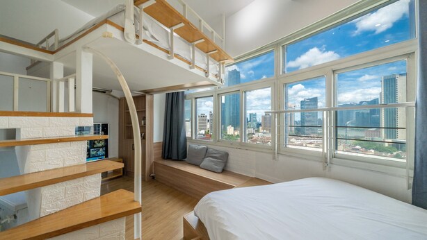 Un dormitorio moderno con un altillo para dormir, un ventanal con vista a la ciudad y un banco empotrado con espacio de almacenamiento.