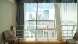 Habitación de hotel con un ventanal grande, dos sillas y vista a la ciudad.