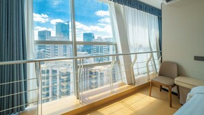 Habitación de hotel con un ventanal amplio que ofrece vistas a la ciudad, una cama, una silla y una mesita.