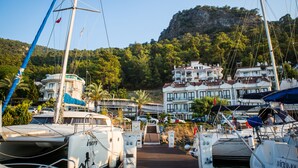 A marina with boats docked, a building with balconies, and a mountainous backdrop. - Ata Park Hotel (Fethiye)