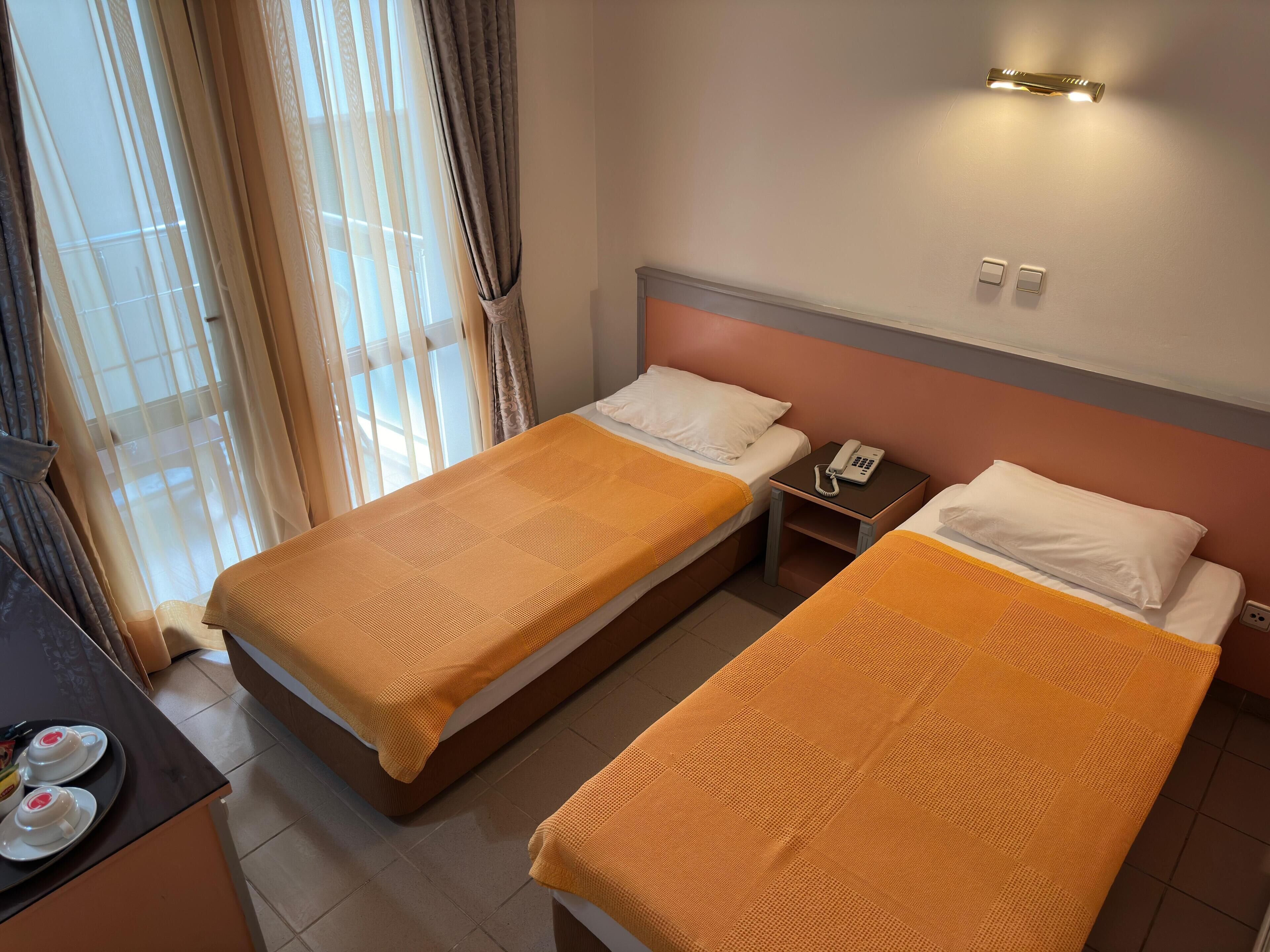 A hotel room with two single beds, a bedside table with a phone, and a window with curtains.