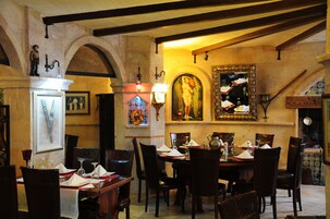 Un comedor con mesas dispuestas para el servicio, obras de arte en las paredes y un techo abovedado.