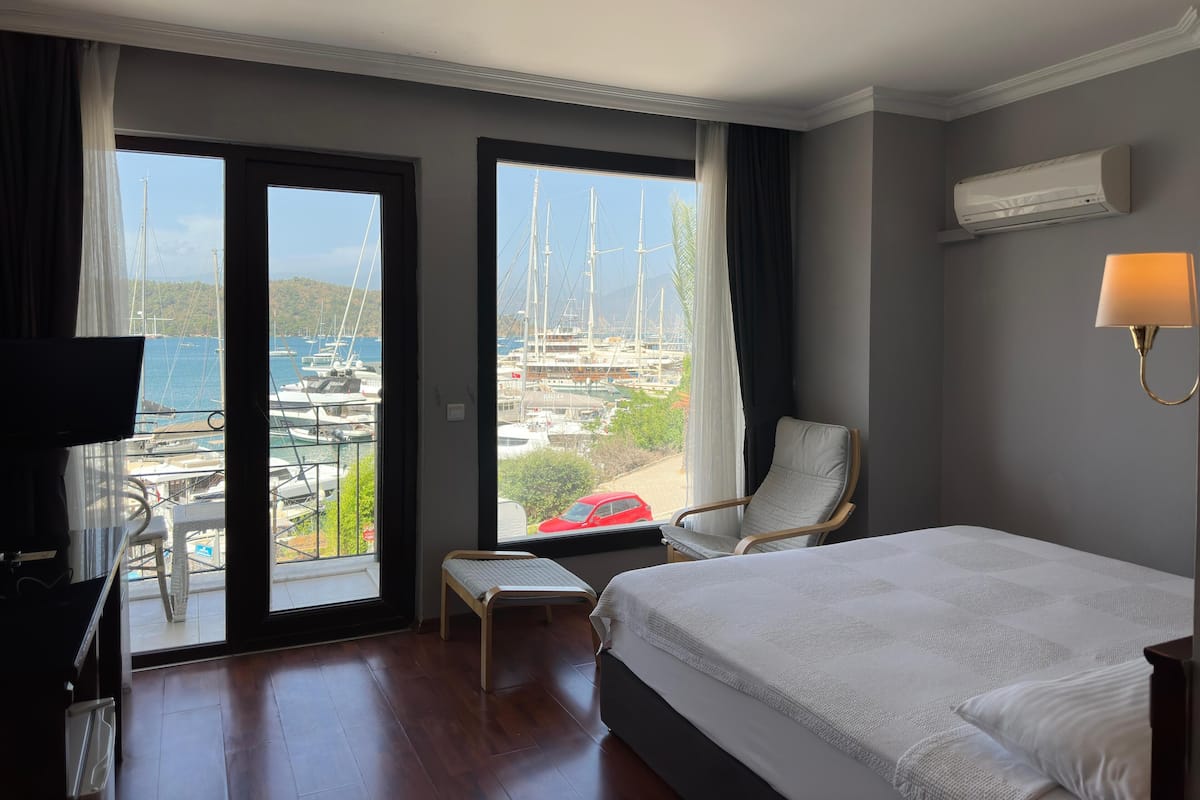 A hotel room with a bed, a chair, a small table, and a view of a marina with boats.
