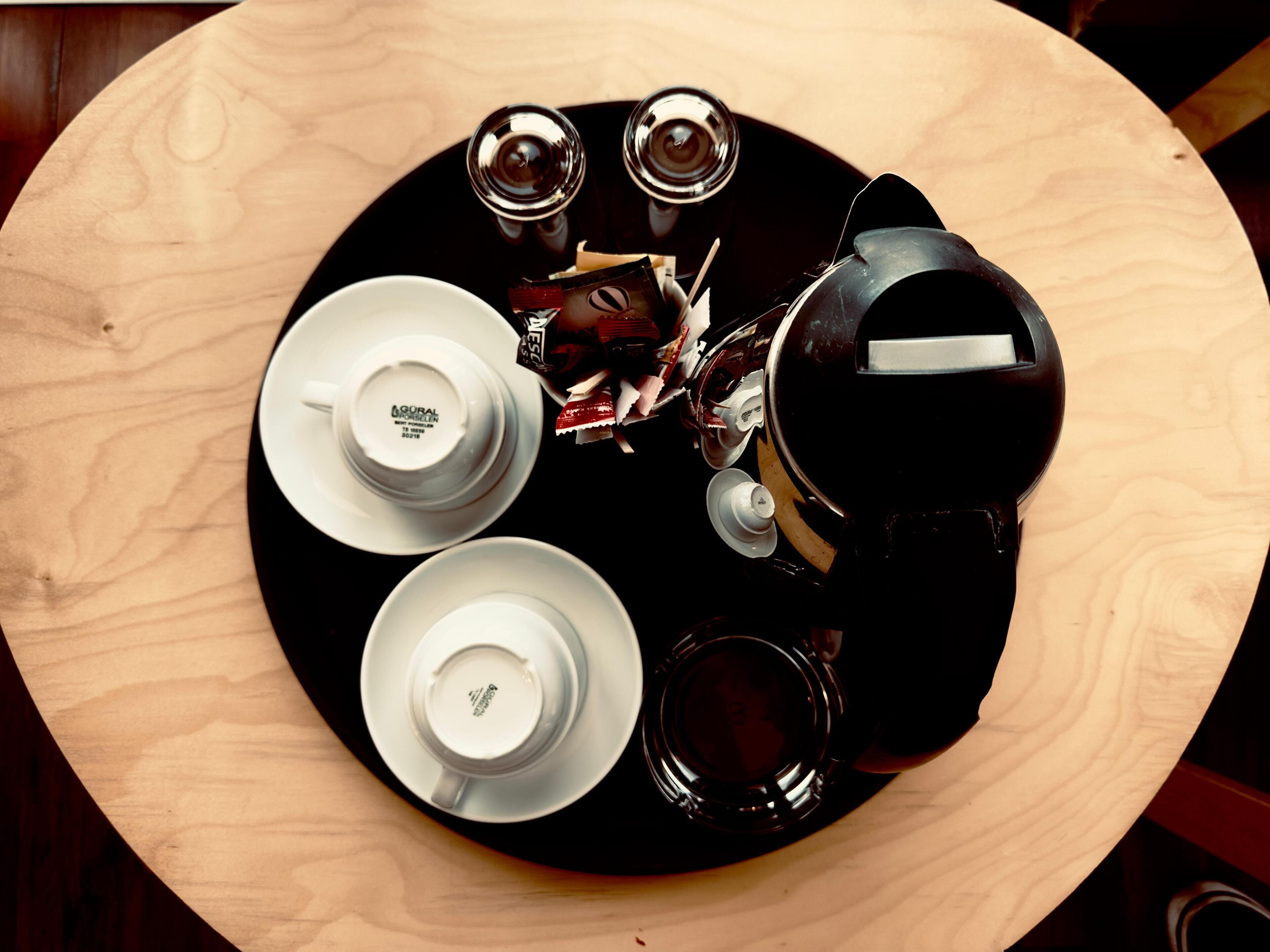 A round wooden table with four white plates, two cups, and a teapot.