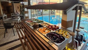 A buffet area with various food options, a pool view, and a wooden bench. - Ata Park Hotel (Fethiye)