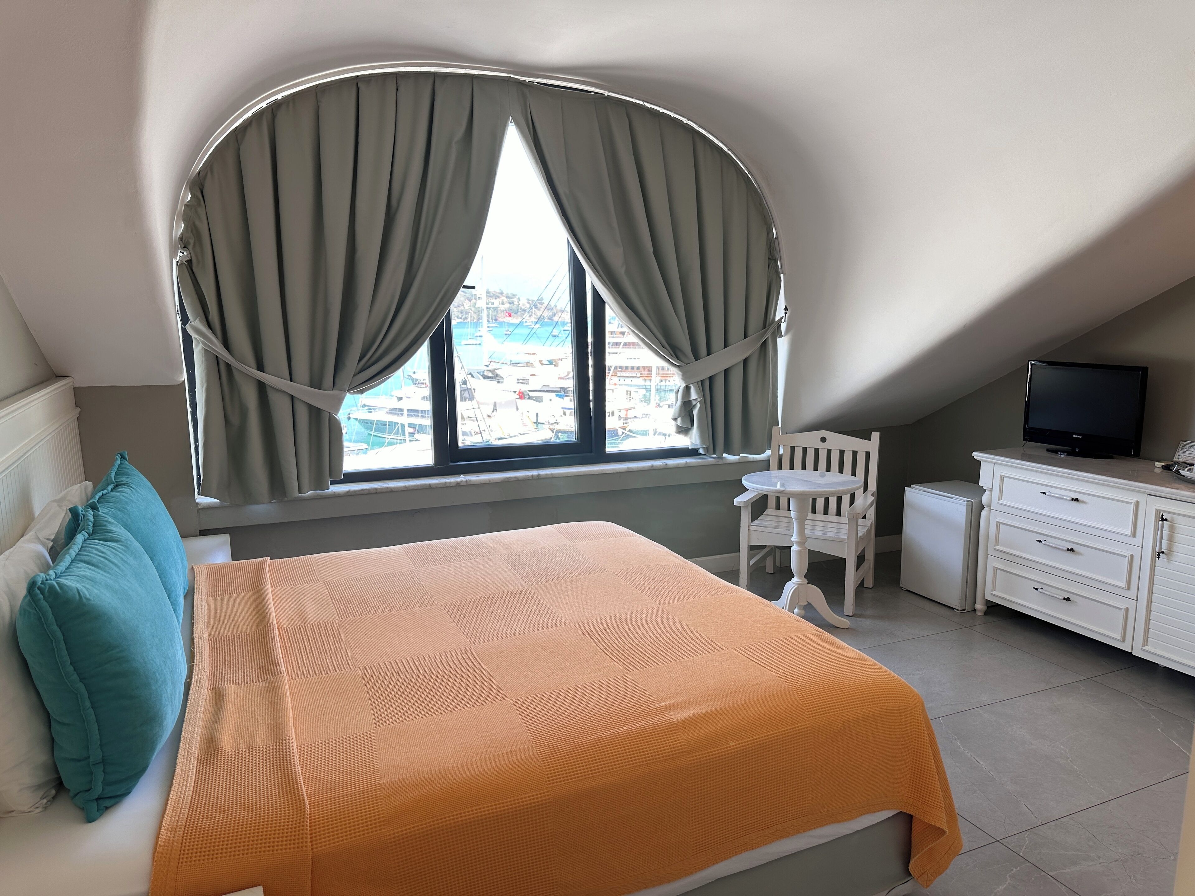 A bedroom with a bed, a chair, a TV, and a window with curtains.