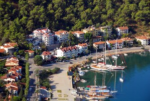 Un pueblo costero con edificios de varios pisos, un puerto deportivo con barcos y una carretera que conduce al frente marítimo.