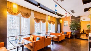 A modern hotel lobby with orange sofas, a glass coffee table, and large windows offering city views.