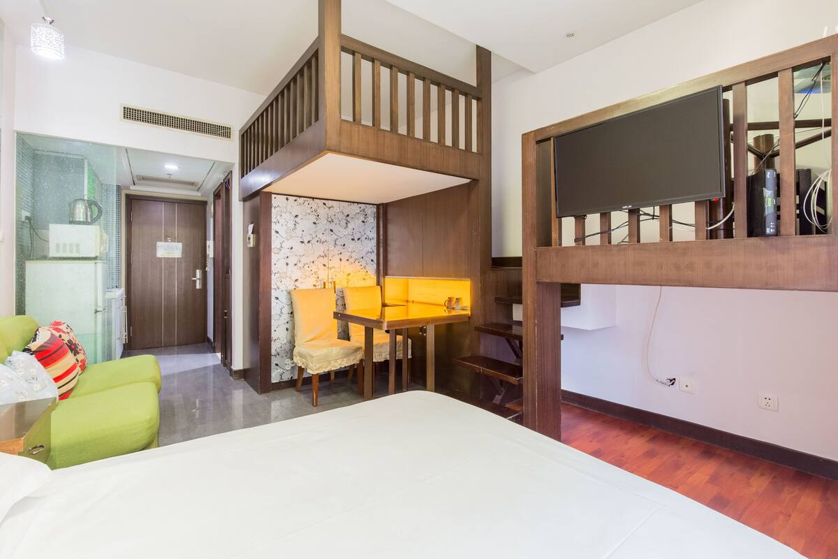 A hotel room with a bunk bed, a desk with a chair, a small table, and a television.