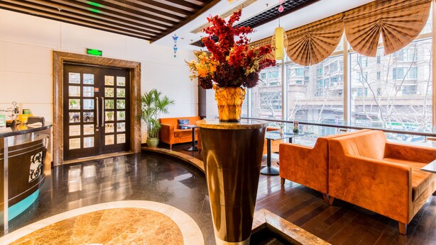 A lobby with a reception desk, a large vase of flowers, orange sofas, and a large window with a view of the city.