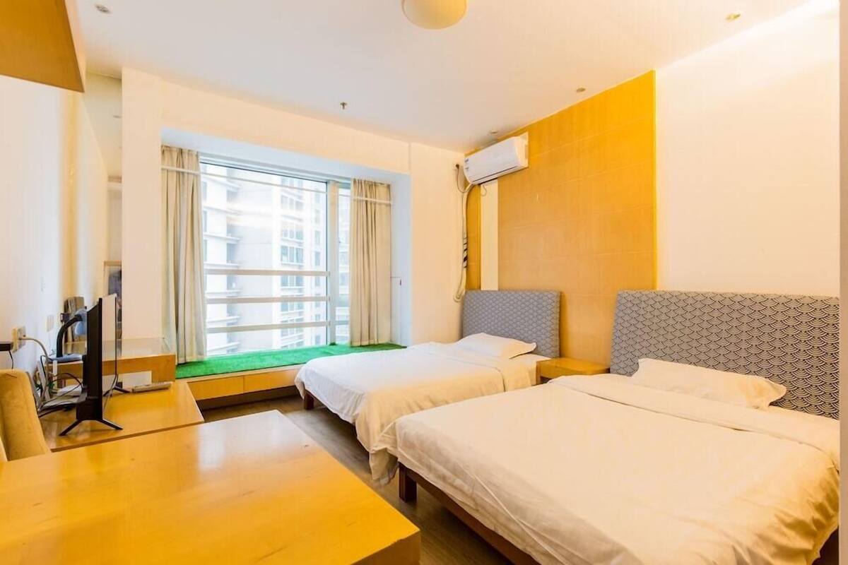 A hotel room with two beds, a desk, a computer, and a window with curtains.